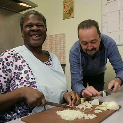 Woman smiling whilst male support worker helps her with cooking tasks
